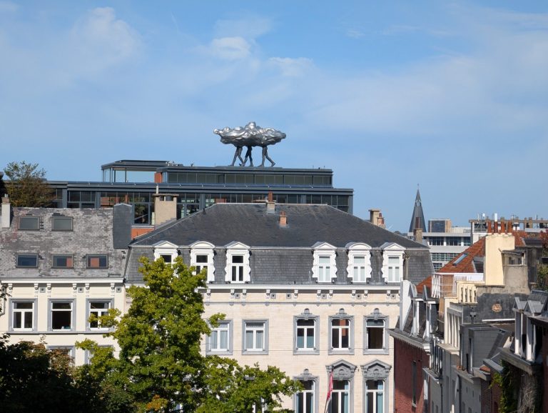 View of city rooftops with a modern building structure in the background under a blue sky.