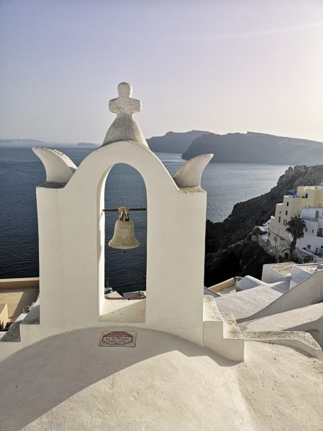 A white bell tower overlooking the sea and hills of Santorini, Greece.