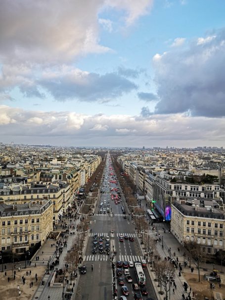 View of a wide boulevard lined with buildings under a cloudy sky in a city.