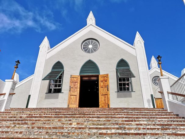 Facade of a St Peter's church in Bermuda with wooden doors, pointed arches, and a blue sky.