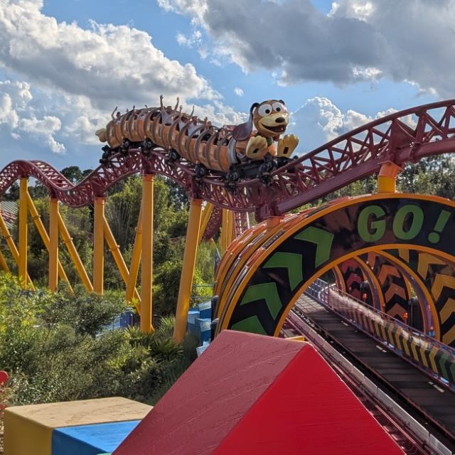 Colourful roller coaster track with vibrant structures under a cloudy sky.