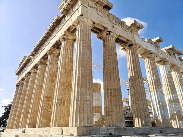 The Parthenon at the Acropolis in Athens, with tall columns against a clear blue sky.