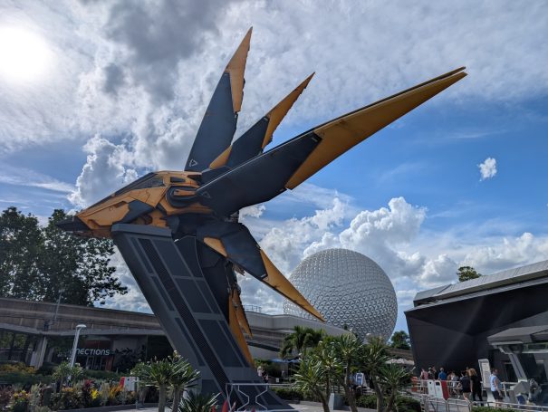 A large, angular sculpture with black and orange features, set against a blue sky and clouds. Located at Disney's Epcot.