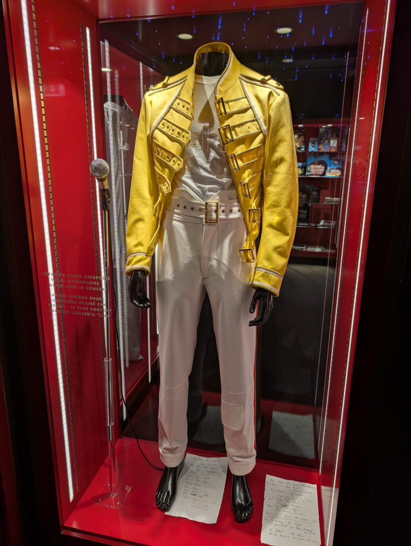 Gold military-style jacket with white trousers on a mannequin in a display case.