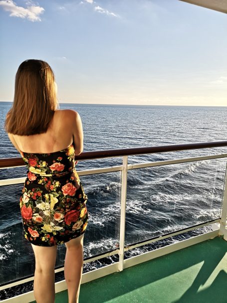I&B's Founder posing in a floral dress on a cruise ship balcony looking out at the ocean.