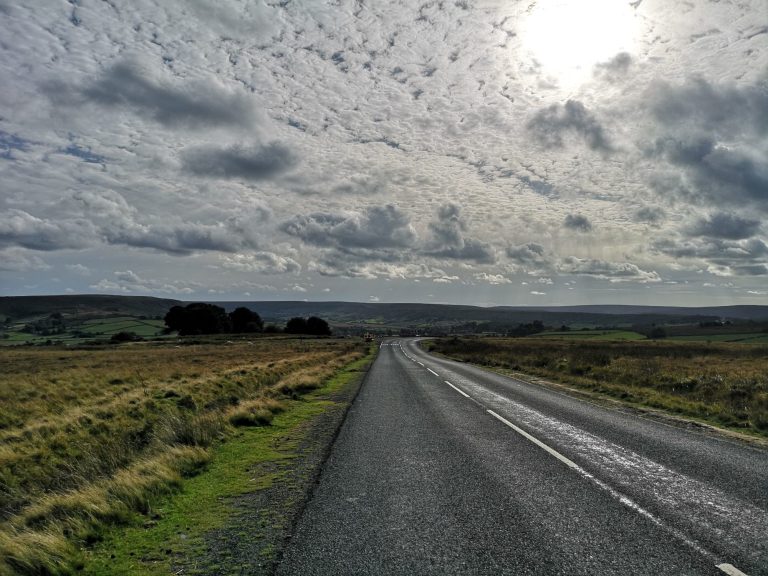 A winding road through open fields under a cloudy sky.