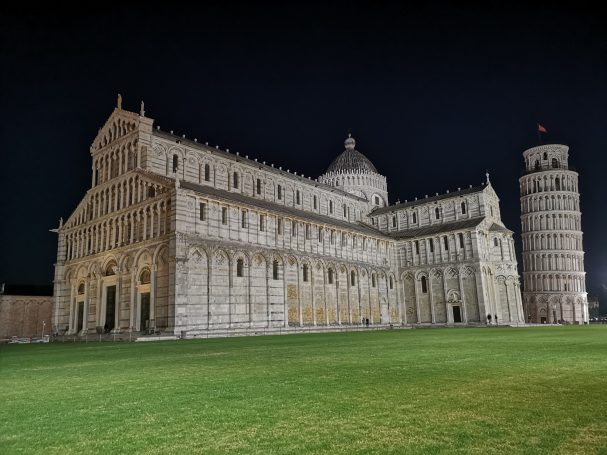 Cathedral and Leaning Tower of Pisa illuminated at night, set against a dark sky.
