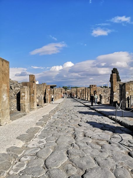 Ancient cobblestone street of Pompeii lined with ruins under a blue sky.