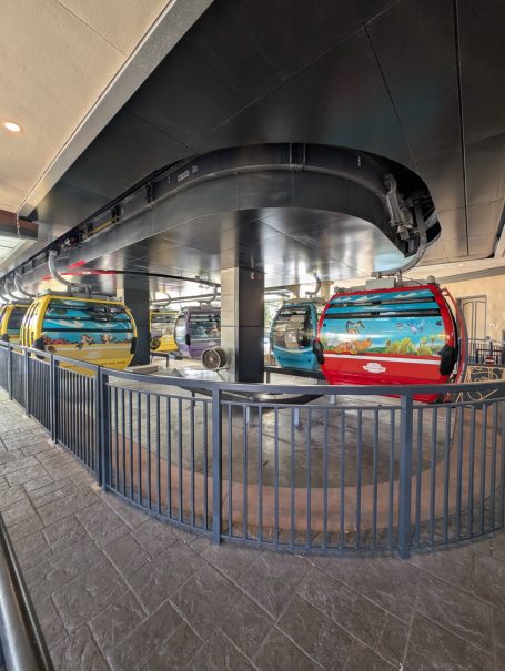 A brightly coloured gondola station with a covered waiting area and cable lines visible.