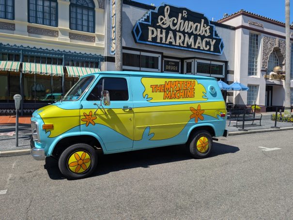 Bright blue and yellow vintage van parked outside a pharmacy, featuring playful graphics.