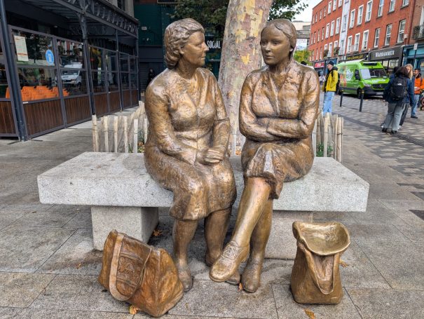Two bronze statues of women seated on a bench, engaged in conversation.