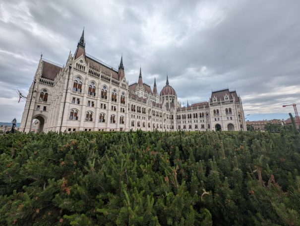 Hungarian Parliament Building with tall spires, surrounded by greenery under a cloudy sky.
