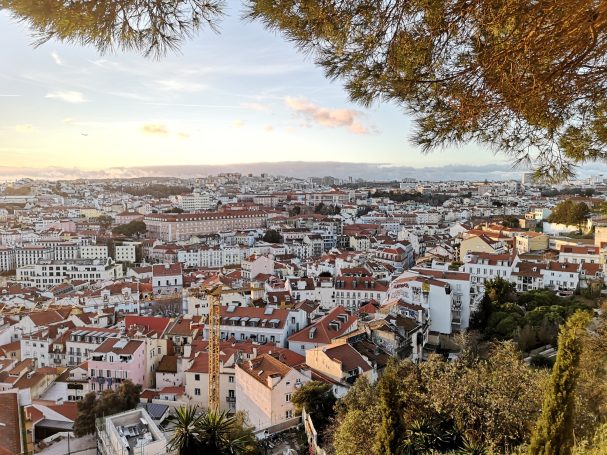 Panoramic view of Lisbon from Miradouro de Santa Luzia, featuring white buildings and red rooftops under a sunset sky.