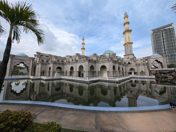 The Federal Territory Mosque in Kuala Lumpur with tall minarets reflected in a serene pool, surrounded by palm trees.