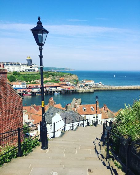 Coastal view with a harbor, houses, and a street lamp under a clear blue sky.