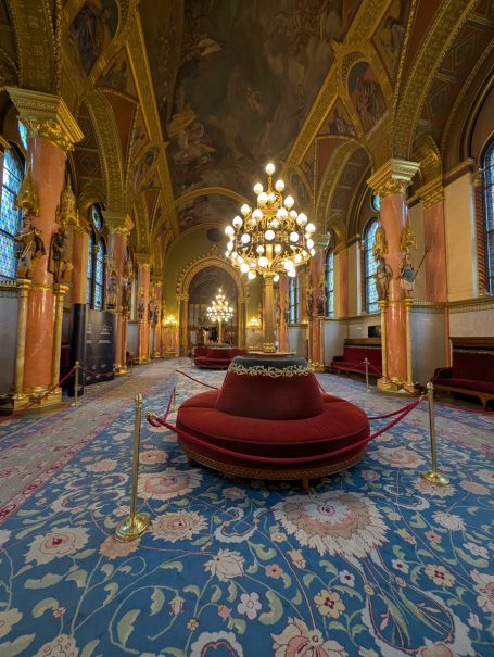 Grand interior with ornate ceiling, chandelier, and plush seating in The Lounge of the Chamber of Peers.