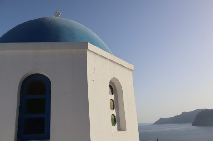 White architecture with a blue dome overlooking the serene coastal landscape of Oia in Santorini.