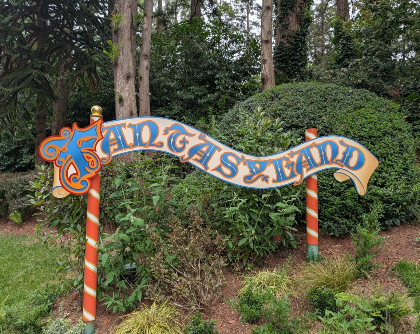 Colourful "Fantasyland" sign surrounded by greenery and bushes.