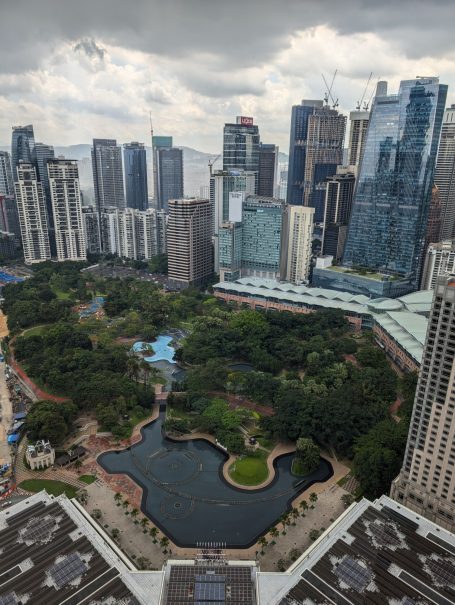 Kuala Lumpur skyline with buildings surrounding the KLCC park and a small lake. Overcast sky.