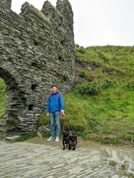 I&B's Founder's Husband and two little dogs with some of Tintagel Castle in the background