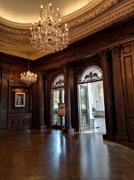 Reception area with ornate chandeliers, wooden panelling, and large doorways, located at Casa Loma in Toronto.