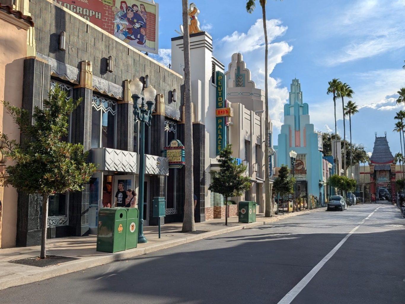 Street scene with palm trees and art deco buildings under a blue sky.