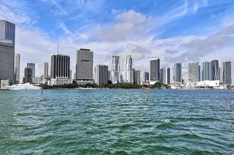 Miami skyline with modern buildings along a waterfront under a blue sky.