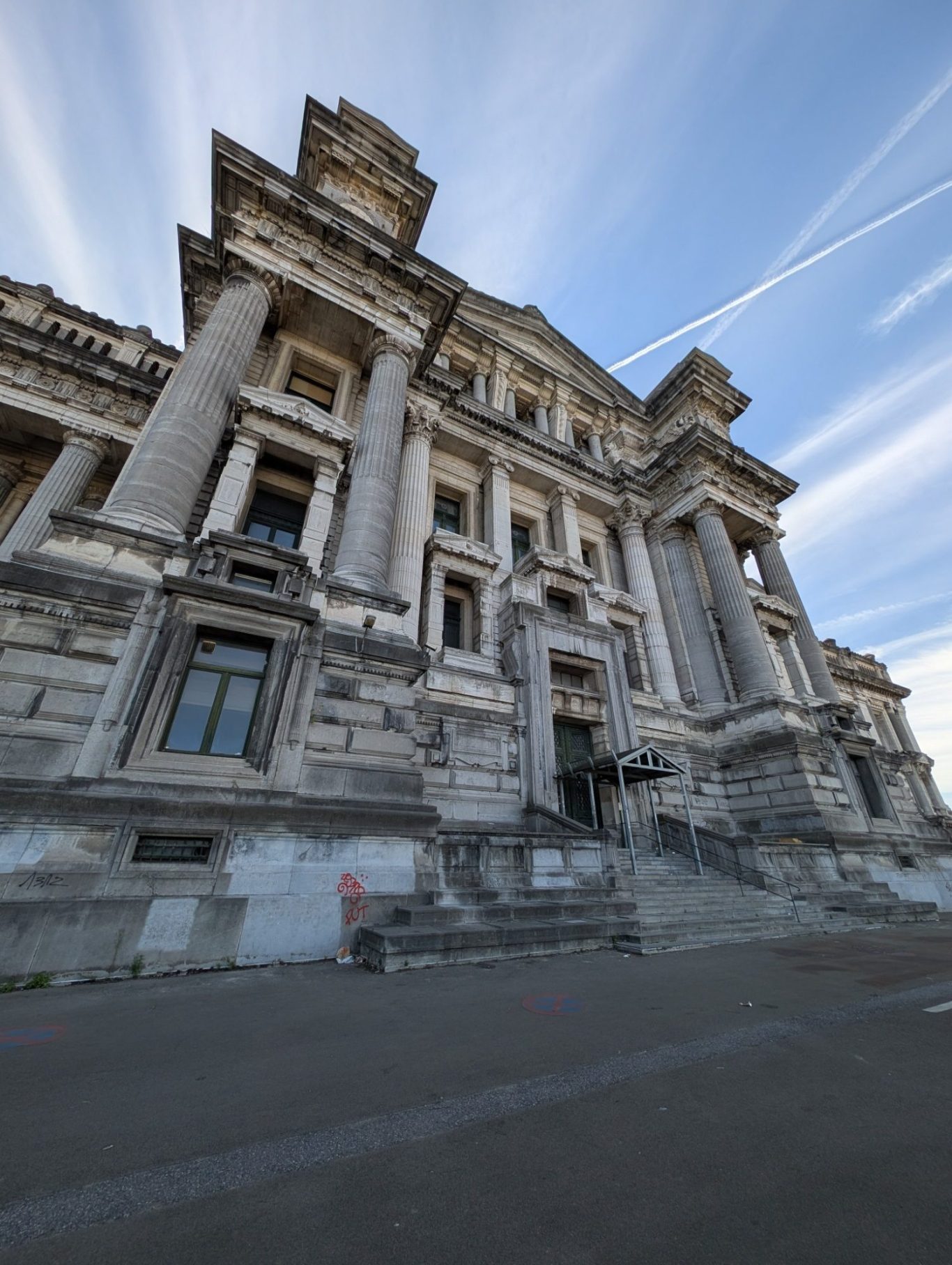 Grand neoclassical building with ornate columns and a large staircase under a blue sky.