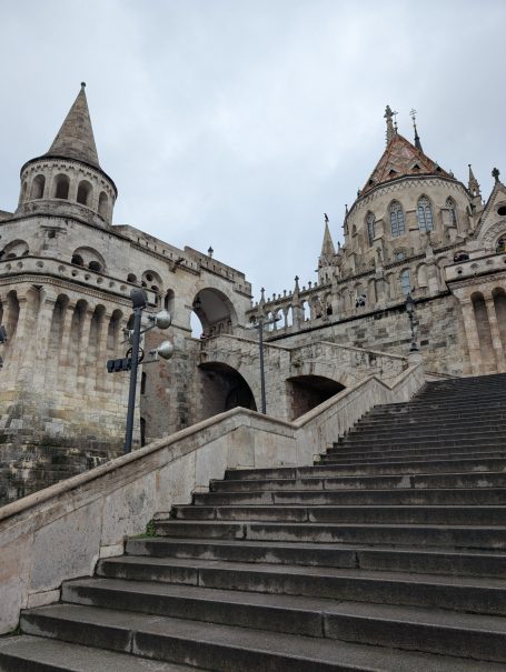 Historic architecture of Fisherman's Bastion in Budapest featuring ornate towers and staircases under a cloudy sky.