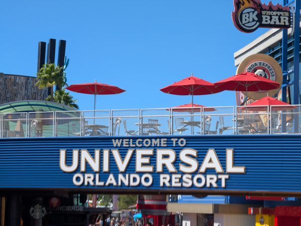 Sign welcoming visitors to Universal Orlando Resort, featuring red umbrellas and clear blue skies.