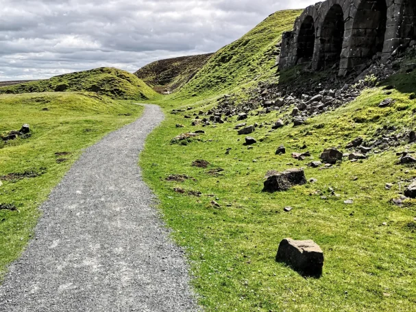A gravel path winding through green hills with old stone arches nearby.