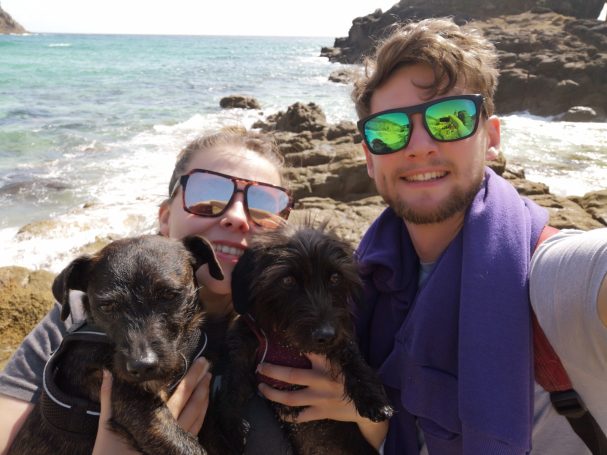 I&B's Founder & Husband holding two little black dogs named Cole & Daisy on Nanjizal Beach in Cornwall