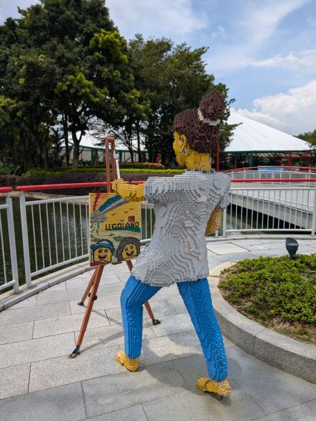 A Lego woman painting on an easel by a tranquil pond, surrounded by greenery at Legoland Malaysia