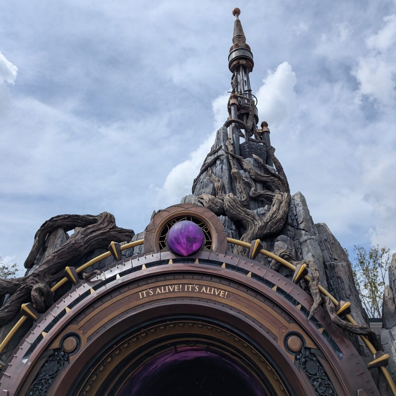 A tall, ornate tower with a circular portal at its base against a cloudy sky.