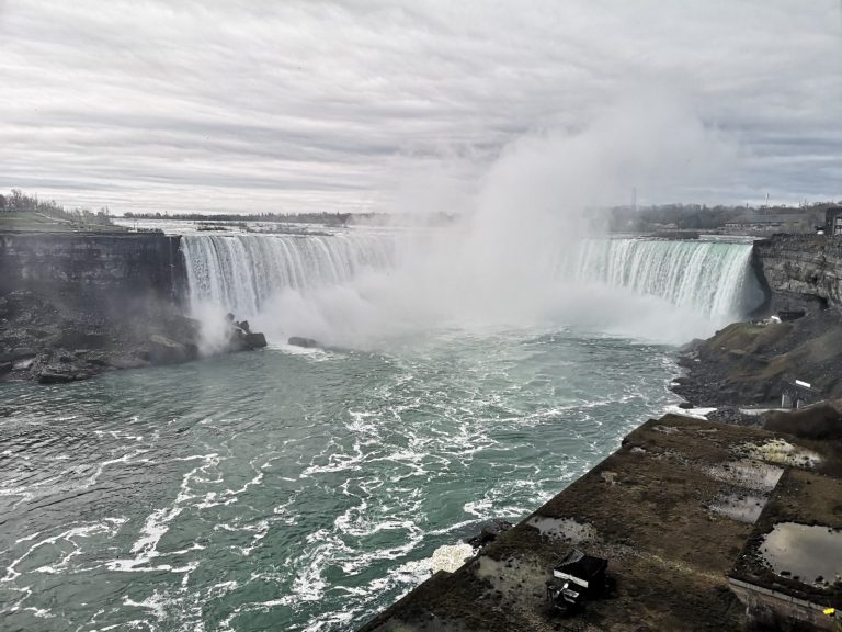 Niagara Falls cascading with mist over rocky terrain under a cloudy sky.