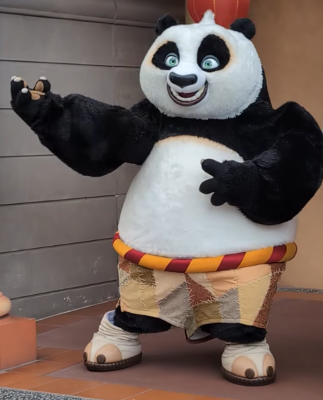 A cartoon panda character wearing shorts and holding a small object, smiling cheerfully.