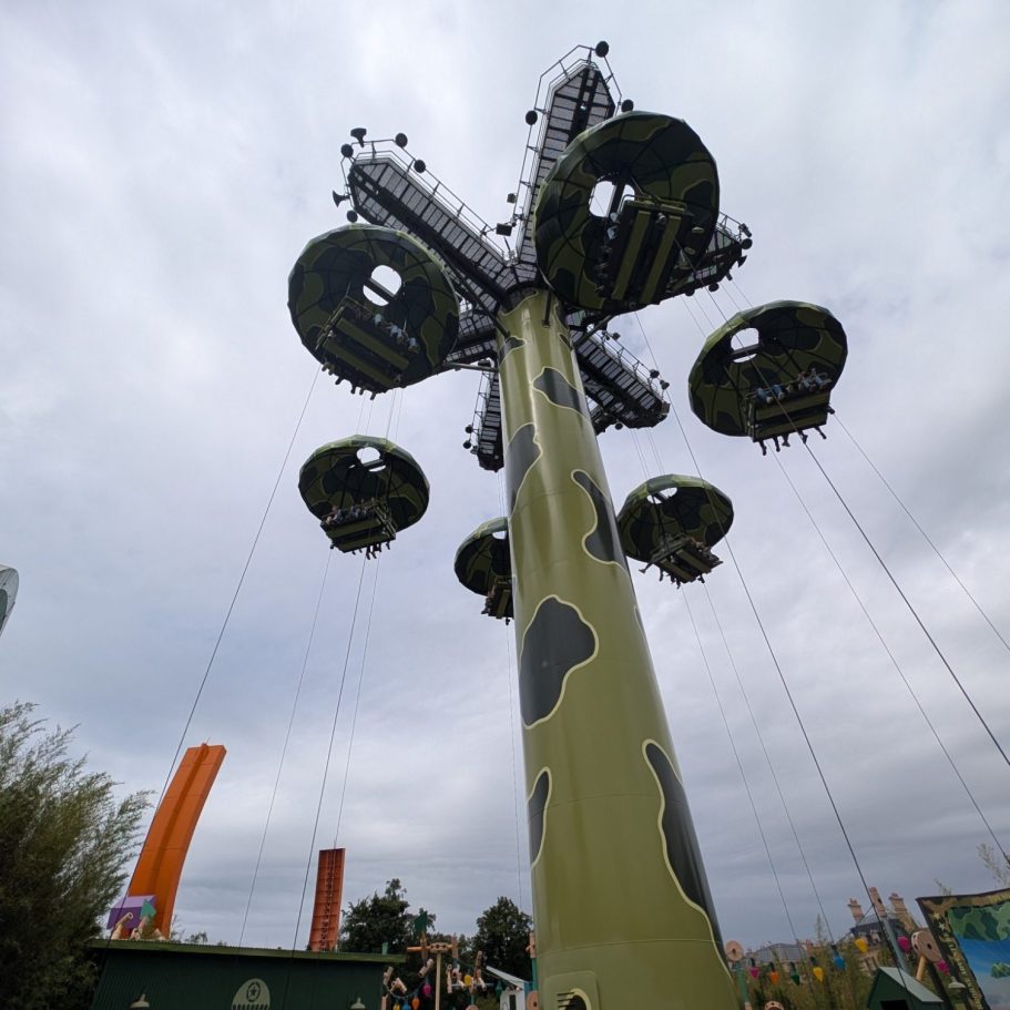 Tall ride structure with circular seating pods suspended from a green, patterned pole.