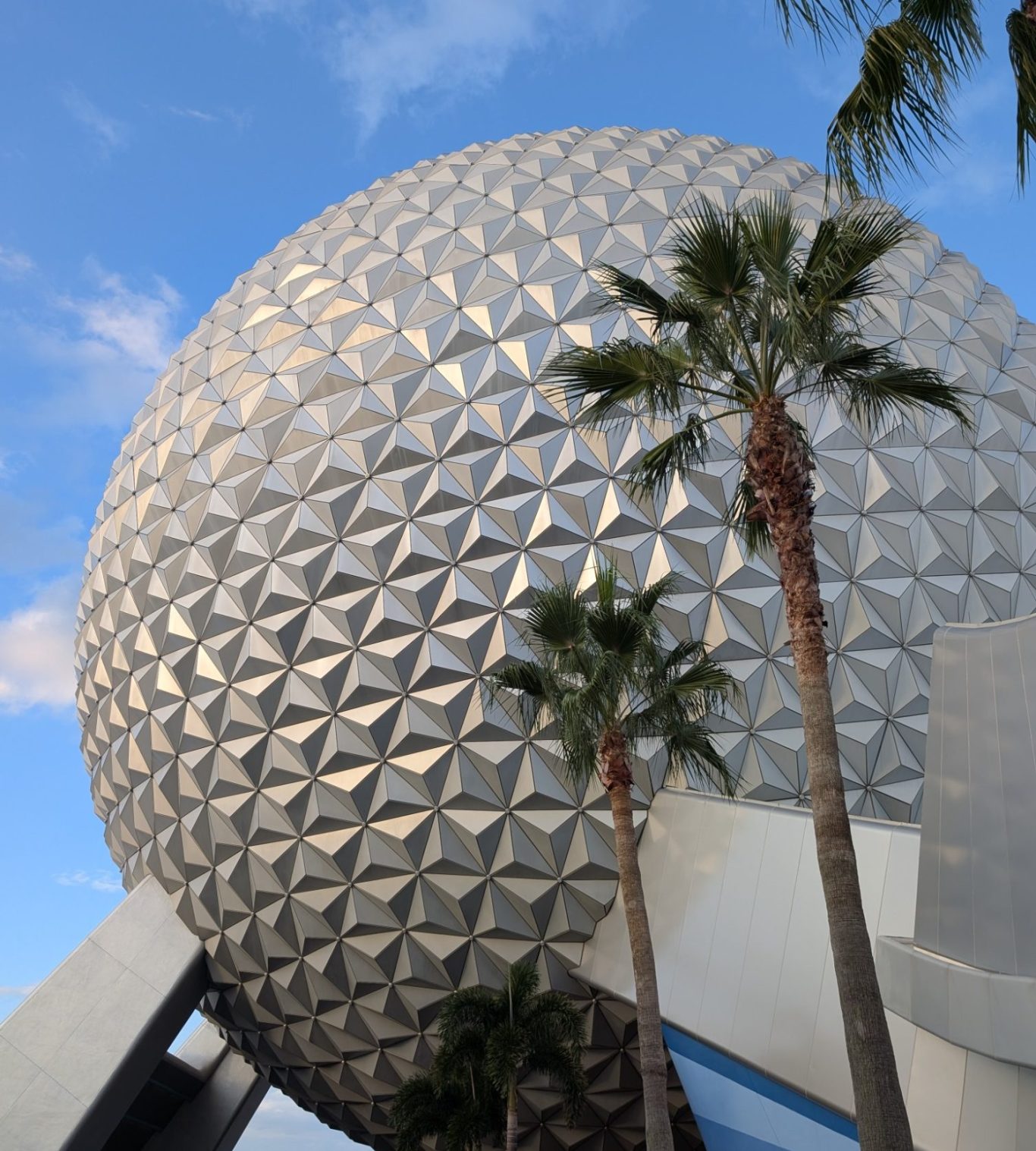 Geodesic dome structure surrounded by palm trees against a blue sky.