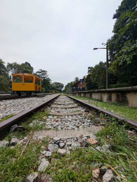 View of railway tracks with a yellow train and lush greenery beside the line, located on Singapore's Rail Corridor.