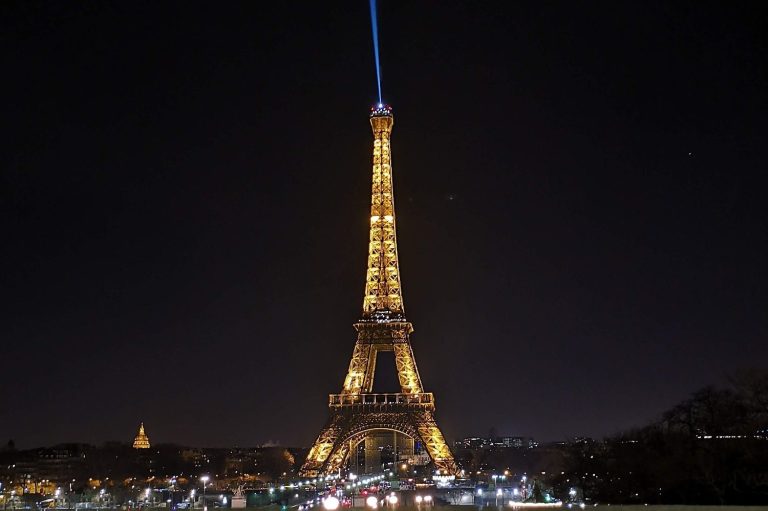 Eiffel Tower illuminated at night with a beam of light shining upwards.