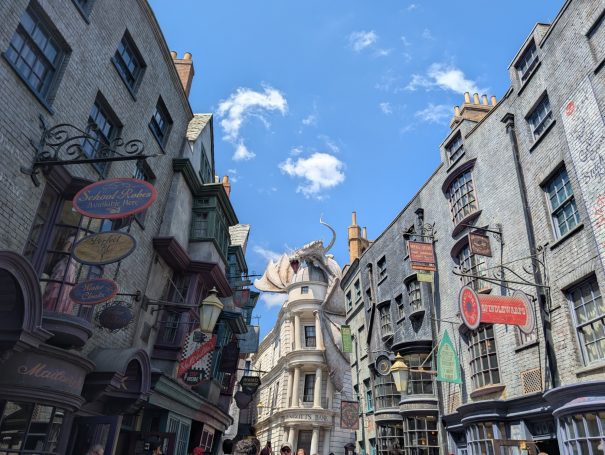 A bustling street scene in a wizarding village with ornate buildings and blue sky.