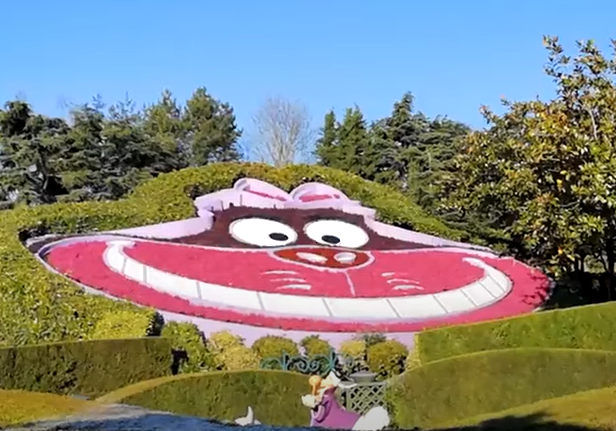 Large floral display of a smiling cat with a pink face and wide grin set against a blue sky.