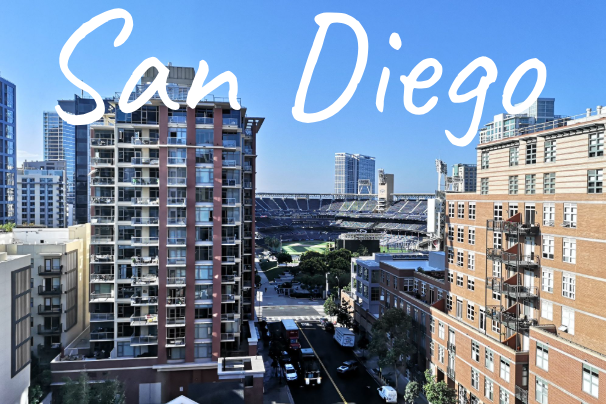 Cityscape of San Diego with modern buildings and a clear blue sky, with Petco Park in the background.
