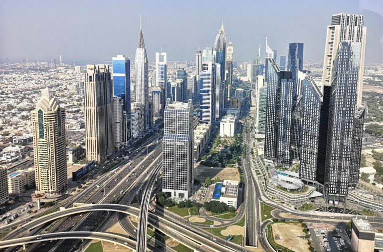 Aerial view of the Dubai city skyline with skyscrapers and busy roads.