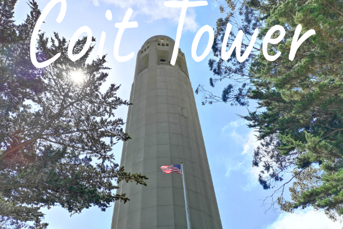 A tall grey tower, known as Coit Tower with an American flag and trees nearby under a blue sky.
