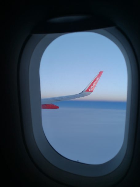 Play Airlines aircraft wing visible through a window, with a clear blue sky in the background.