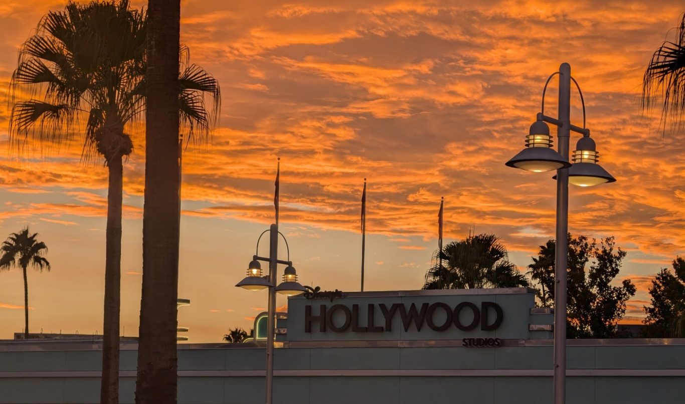 Sunset sky with vibrant orange clouds above a sign for Disney's Hollywood Studios and palm trees.