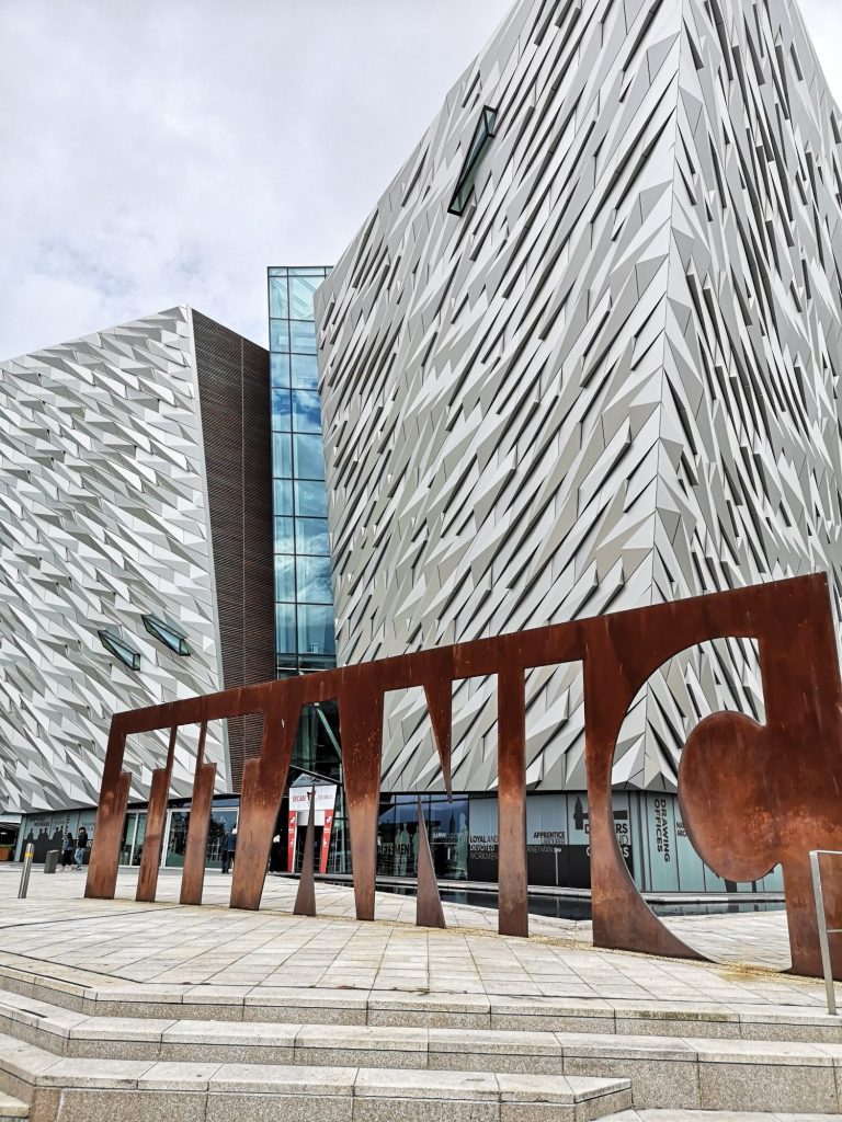 The Titanic Quarter features modern architecture with a large "Titanic" sign in front.