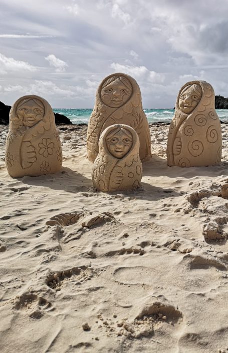 Four carved stone figures on Horseshoe Bay beach, with ocean and clouds in the background.