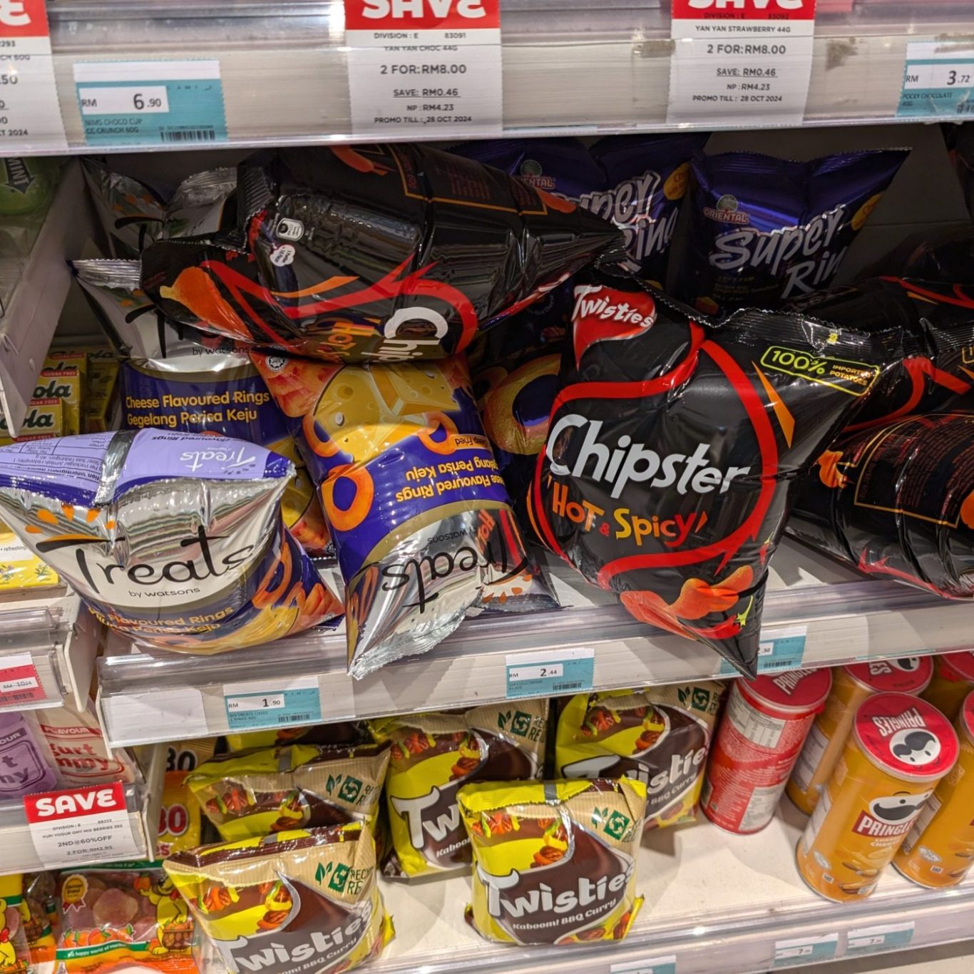 A shelf stocked with various brands of snack crisps and soft drinks.